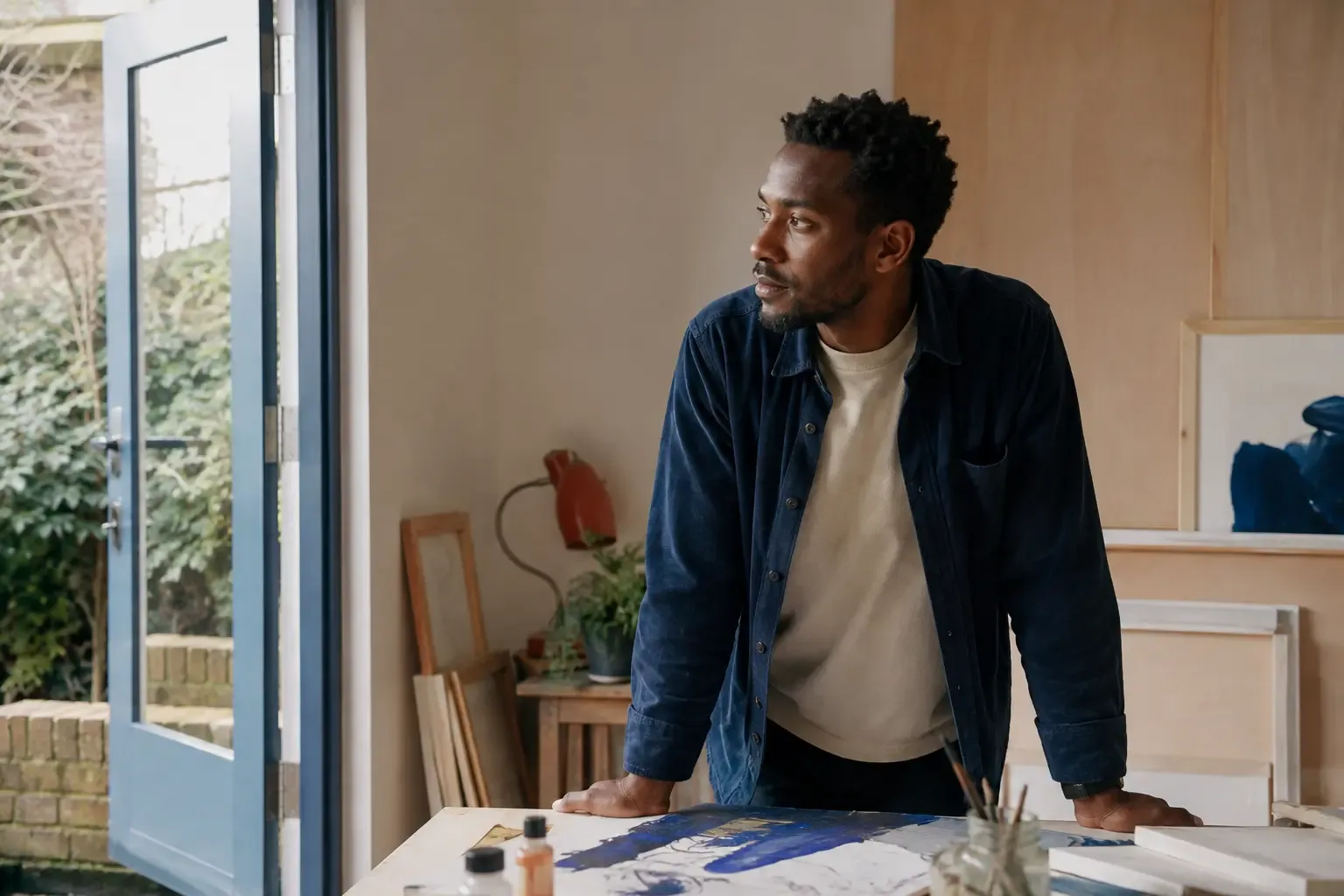 A man pausing beside an unfinished creative project in a studio.