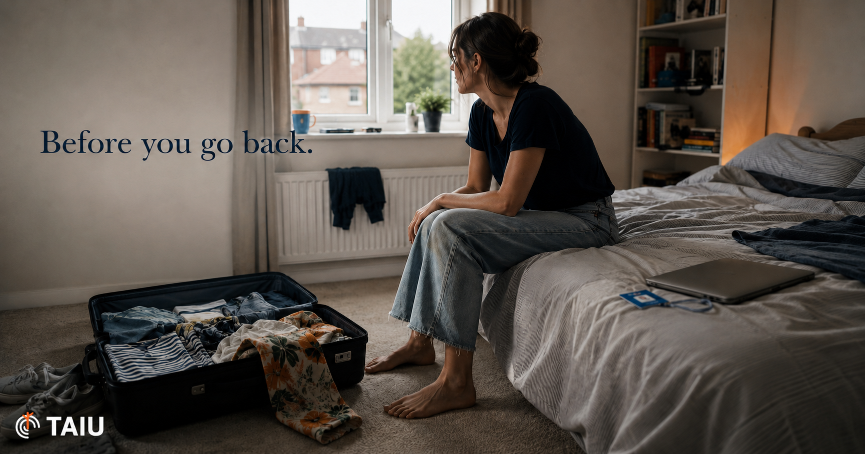 A woman sitting on the edge of her bed beside an open suitcase, looking out of the window before returning to work.