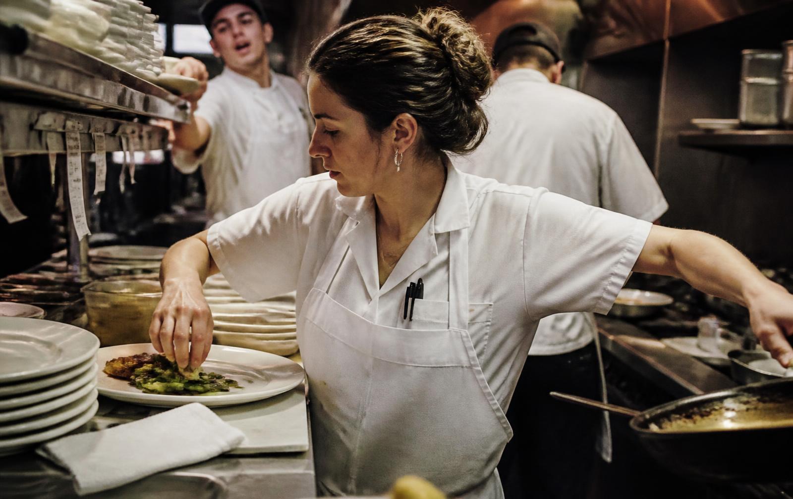 A cook working through service in a busy commercial kitchen, absorbed in the task