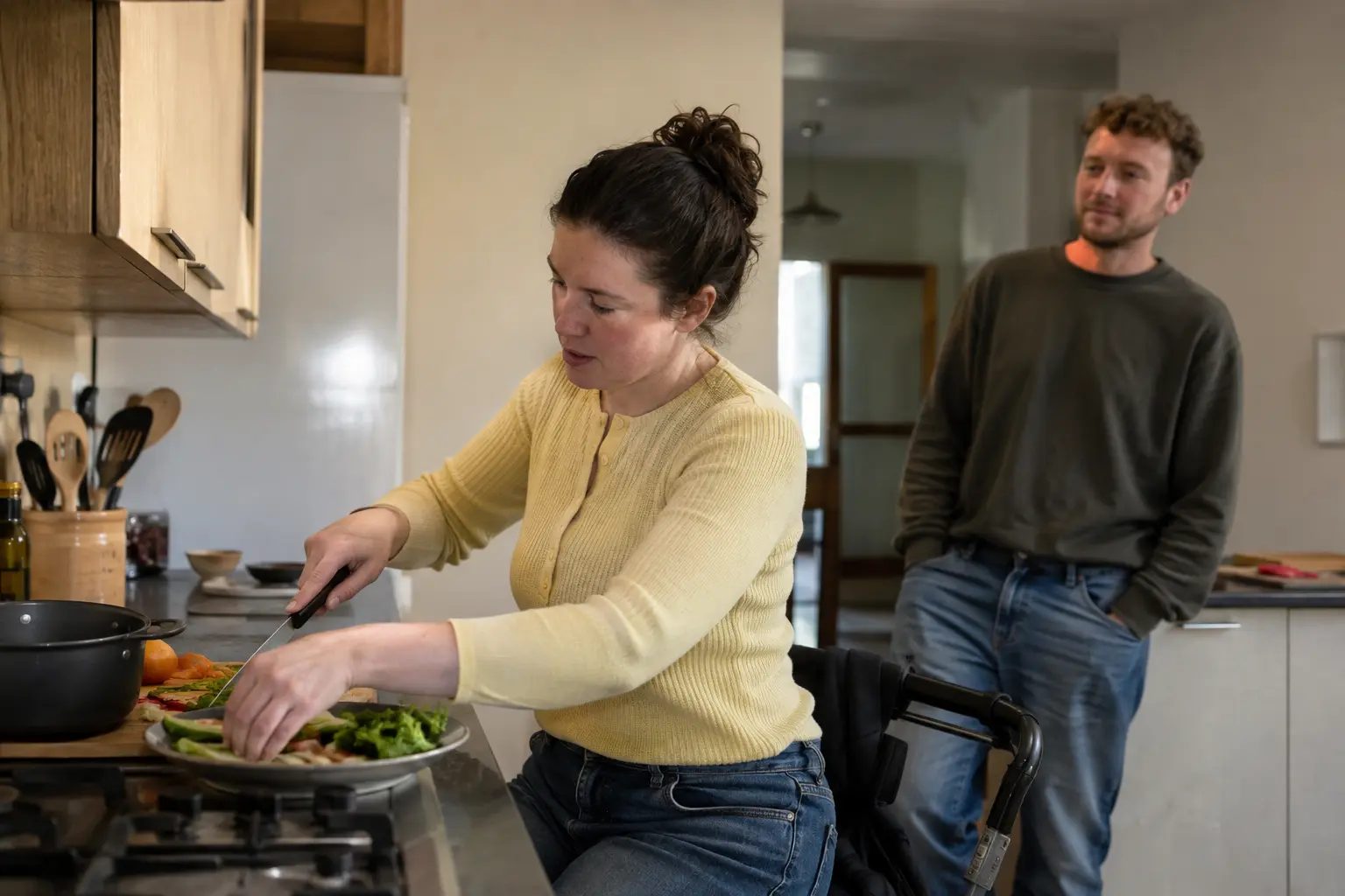 A woman preparing food at her own kitchen counter while a friend stands back and follows her lead