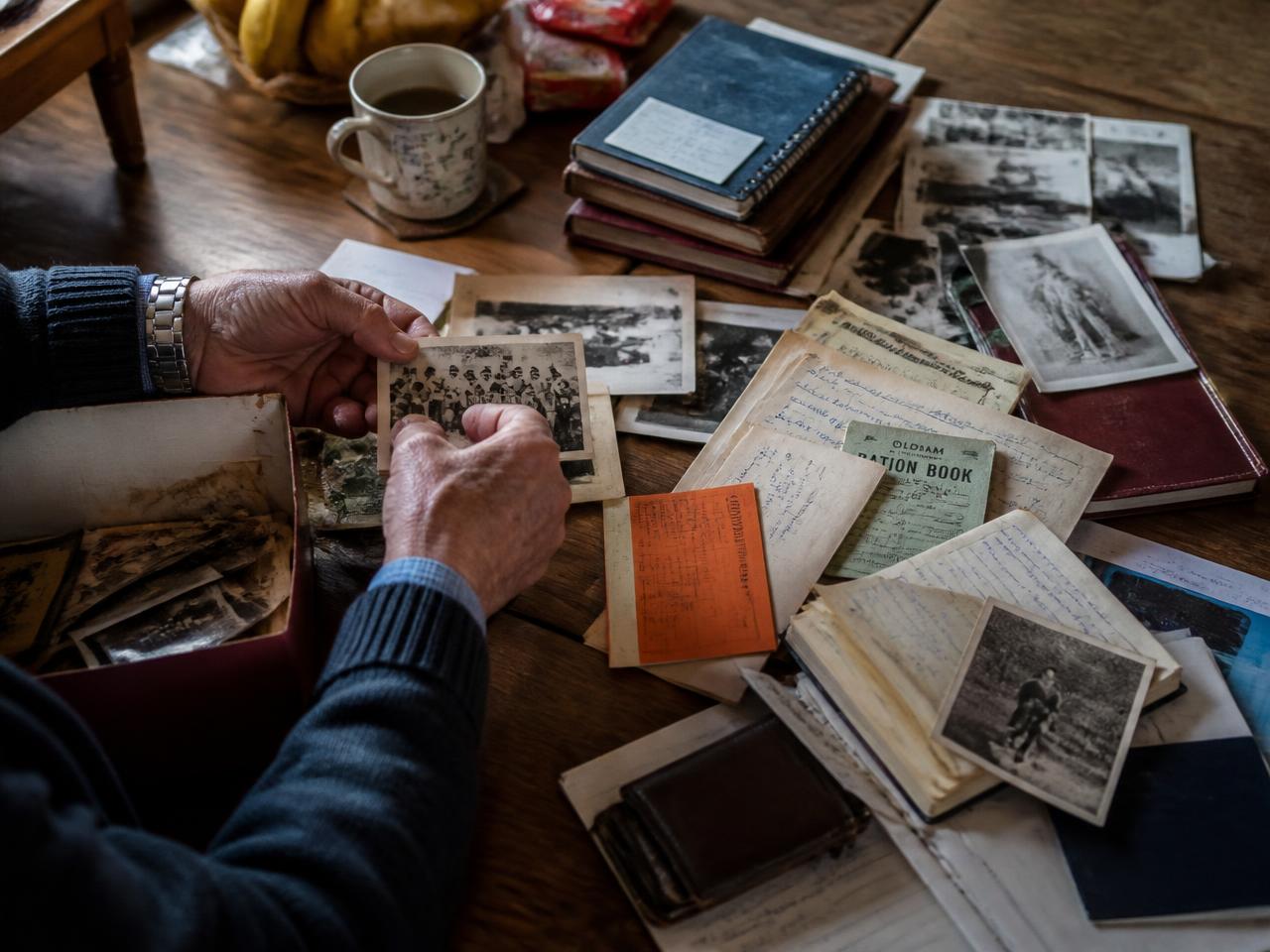 Hands sorting through old photographs, letters and notebooks on a wooden table